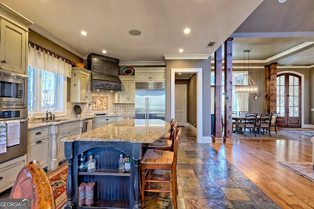 kitchen with a center island, built in appliances, light stone counters, decorative light fixtures, and french doors