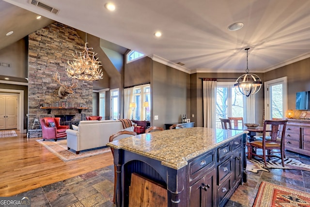 kitchen featuring dark brown cabinetry, decorative light fixtures, a chandelier, a fireplace, and light stone countertops