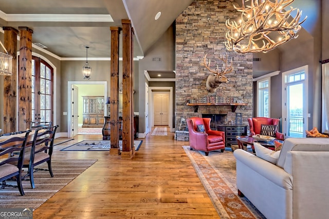 living room with crown molding, a towering ceiling, a stone fireplace, and hardwood / wood-style flooring