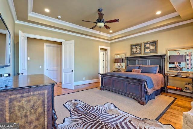 bedroom with ceiling fan, ornamental molding, a tray ceiling, and light hardwood / wood-style flooring