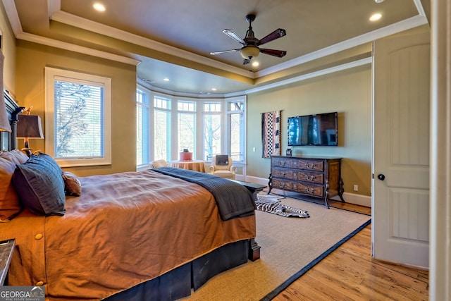 bedroom with multiple windows, light hardwood / wood-style floors, a raised ceiling, and ceiling fan