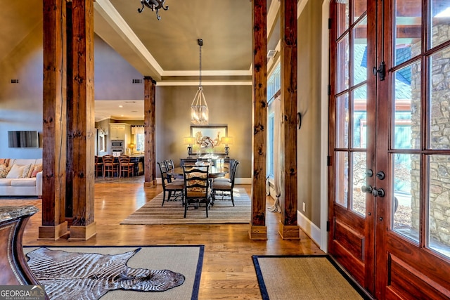 foyer entrance with light hardwood / wood-style flooring, a chandelier, a raised ceiling, crown molding, and french doors