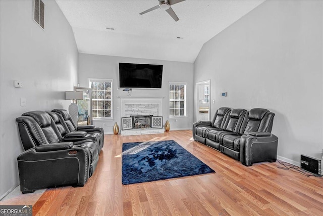 living room featuring ceiling fan, wood-type flooring, a textured ceiling, a brick fireplace, and vaulted ceiling