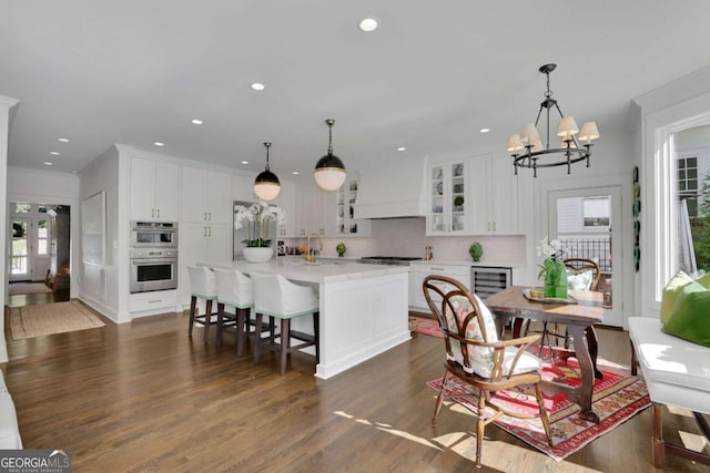 kitchen with appliances with stainless steel finishes, a kitchen island with sink, hanging light fixtures, and white cabinets