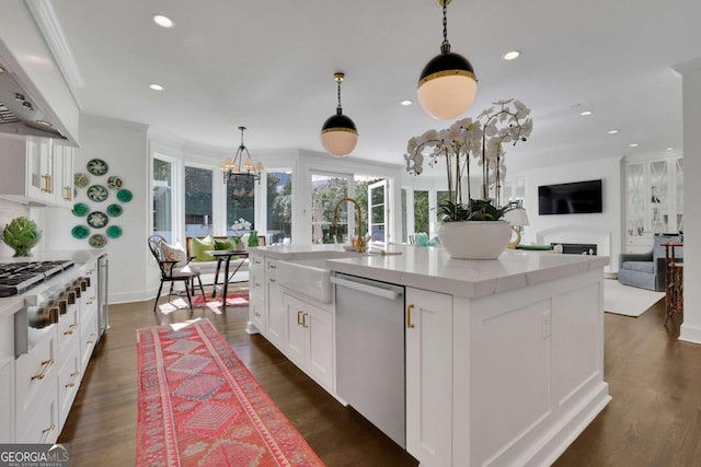 kitchen with appliances with stainless steel finishes, hanging light fixtures, custom range hood, white cabinets, and a center island with sink