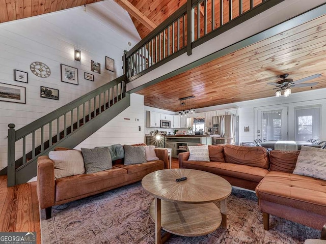 living room with high vaulted ceiling, wood walls, ceiling fan, wooden ceiling, and light hardwood / wood-style flooring