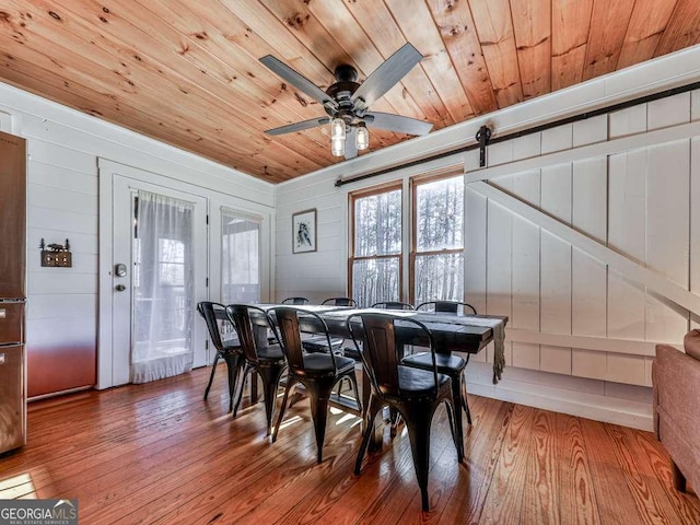 dining room with wooden ceiling, light hardwood / wood-style floors, ceiling fan, and a barn door