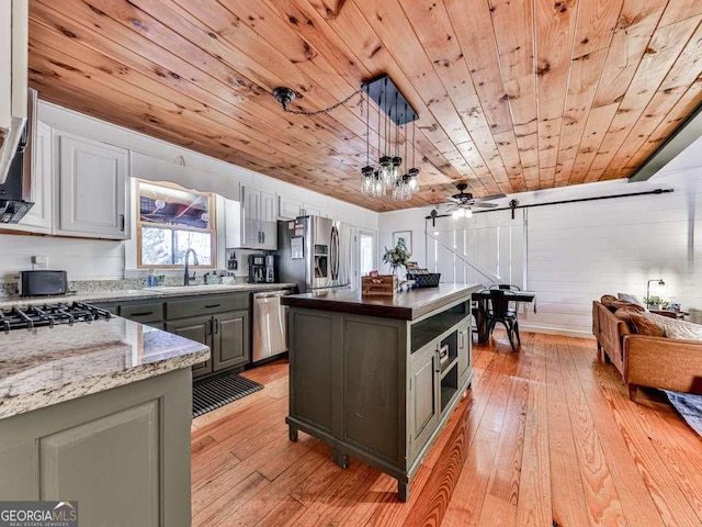 kitchen featuring sink, stainless steel appliances, a kitchen island, decorative light fixtures, and a barn door