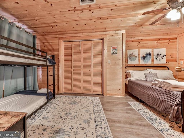 bedroom with light wood-type flooring, wooden ceiling, wooden walls, a closet, and ceiling fan