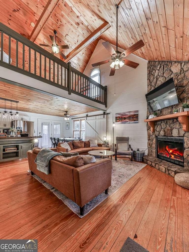 living room with hardwood / wood-style flooring, a stone fireplace, wooden ceiling, and ceiling fan