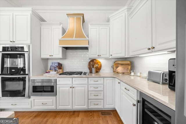 kitchen with wine cooler, tasteful backsplash, appliances with stainless steel finishes, custom range hood, and white cabinets