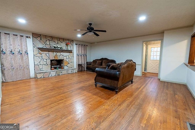 living room with hardwood / wood-style floors, a stone fireplace, ornamental molding, and ceiling fan