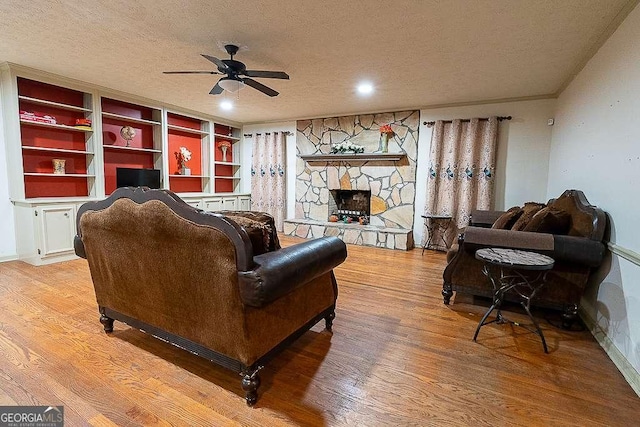 living room featuring ceiling fan, a stone fireplace, a textured ceiling, and light wood-type flooring