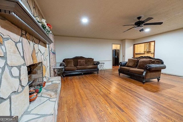 living room featuring crown molding, ceiling fan, wood-type flooring, a fireplace, and a textured ceiling