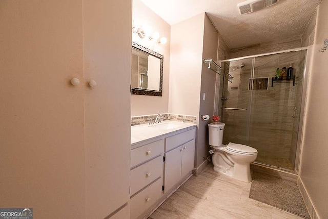 bathroom with vanity, toilet, a shower with shower door, and a textured ceiling