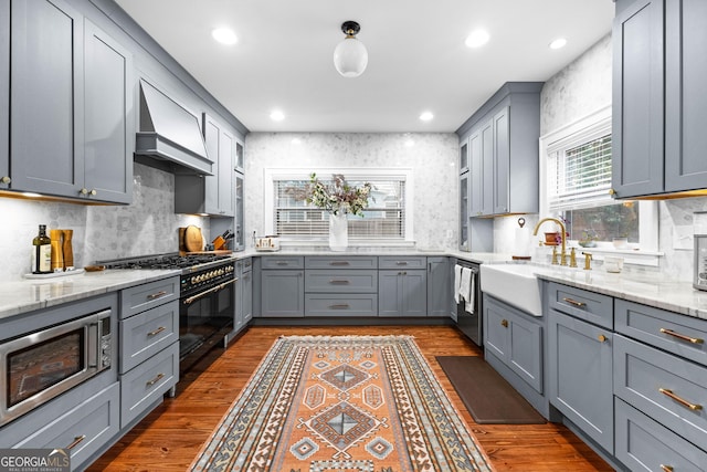 kitchen featuring appliances with stainless steel finishes, sink, gray cabinetry, light stone countertops, and custom range hood