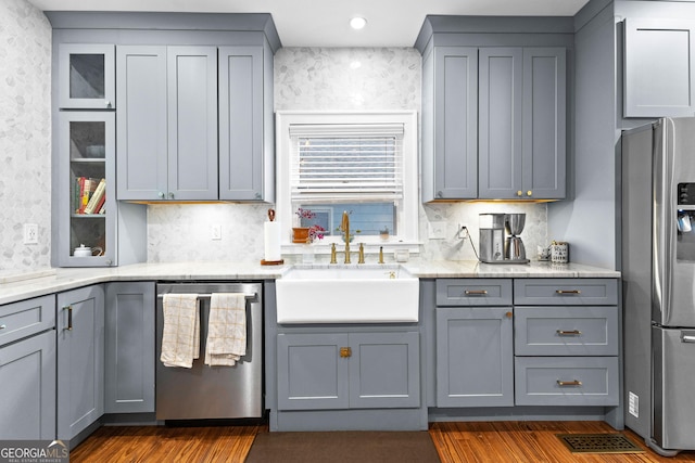 kitchen with stainless steel appliances, gray cabinets, sink, and light stone counters