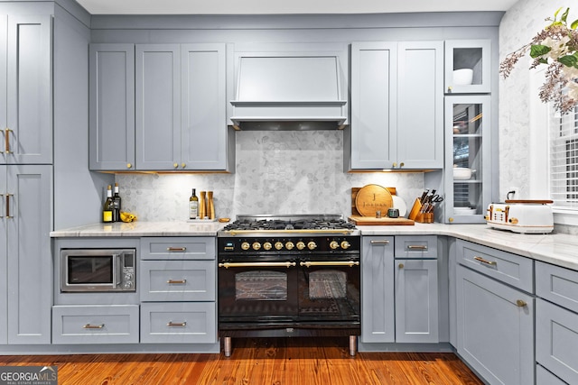 kitchen with gray cabinets, light stone counters, wood-type flooring, custom range hood, and range with two ovens