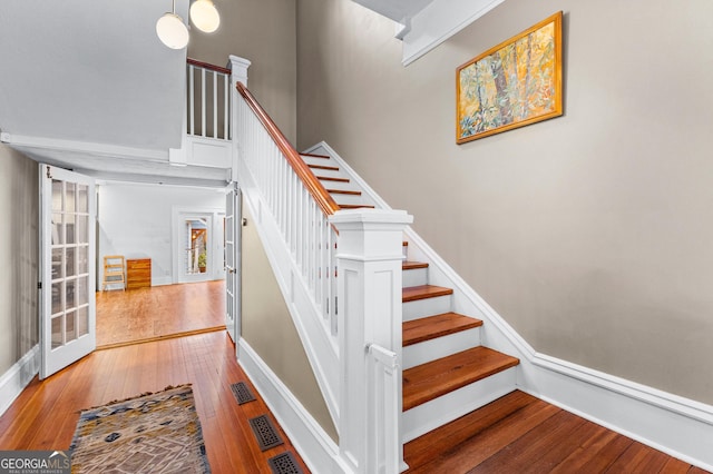 staircase with wood-type flooring, a towering ceiling, and french doors