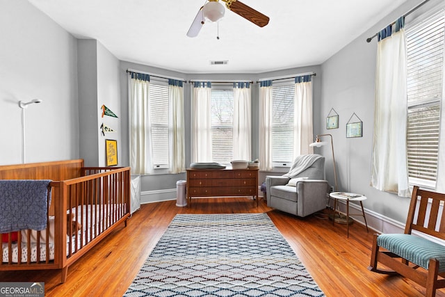 bedroom featuring a nursery area, hardwood / wood-style floors, and ceiling fan