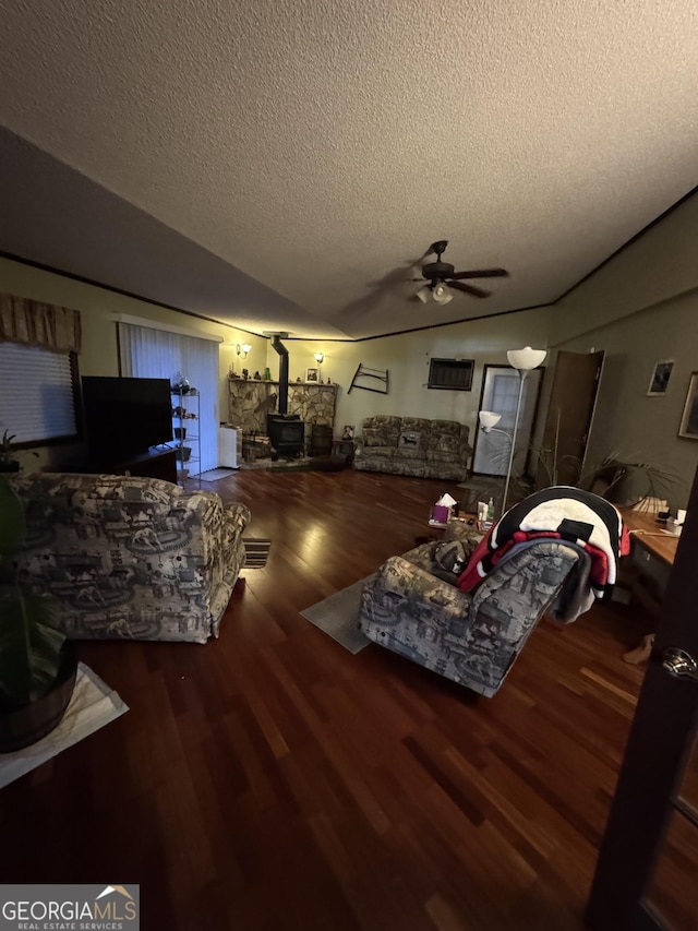 living room with ceiling fan, a wood stove, dark wood-type flooring, and a textured ceiling