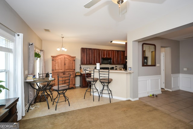 kitchen with ceiling fan with notable chandelier, pendant lighting, a breakfast bar area, light tile patterned floors, and kitchen peninsula