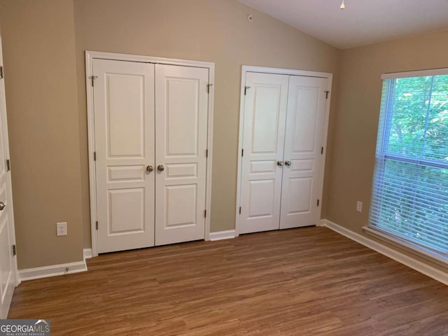 unfurnished bedroom featuring multiple closets, wood-type flooring, and lofted ceiling