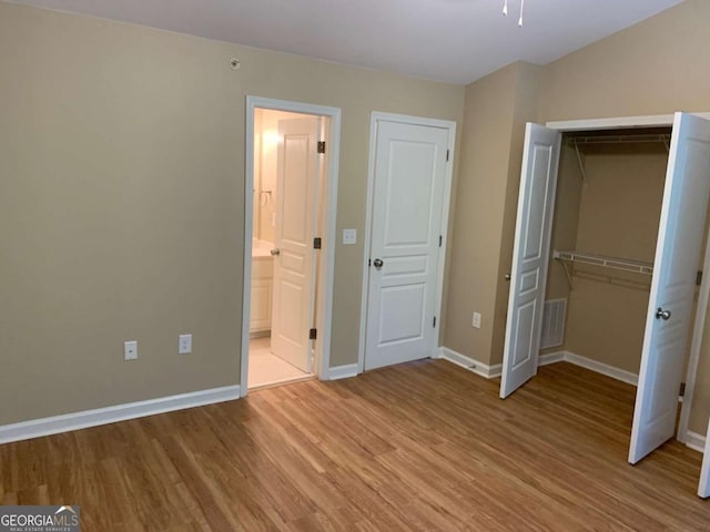 unfurnished bedroom with a closet, ensuite bathroom, and light hardwood / wood-style flooring