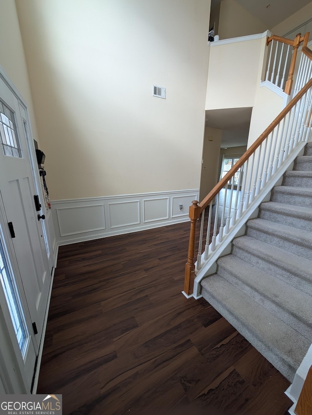 entrance foyer featuring visible vents, a wainscoted wall, stairway, dark wood-type flooring, and a high ceiling