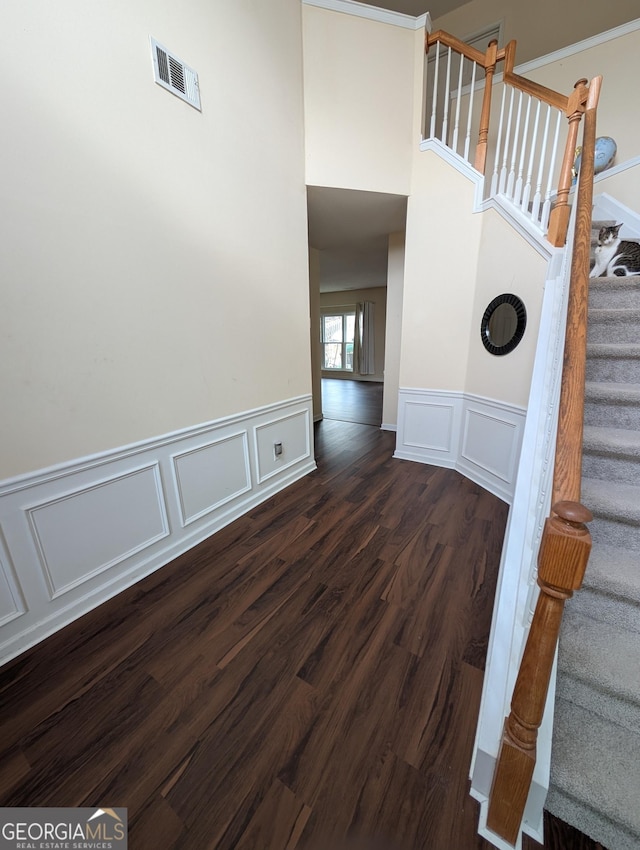 stairway featuring visible vents, a decorative wall, wood finished floors, and wainscoting