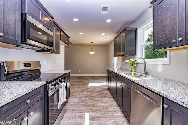 kitchen with sink, stainless steel appliances, light stone countertops, decorative light fixtures, and light wood-type flooring