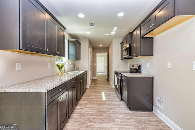 kitchen with sink, light stone counters, dark brown cabinets, light wood-type flooring, and appliances with stainless steel finishes