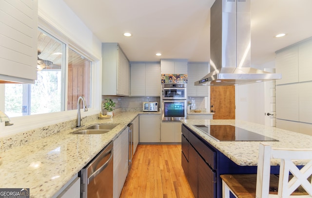 kitchen with light stone counters, island range hood, stainless steel appliances, and sink