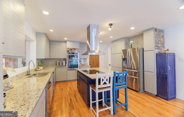 kitchen with sink, island range hood, light wood-type flooring, stainless steel appliances, and light stone countertops