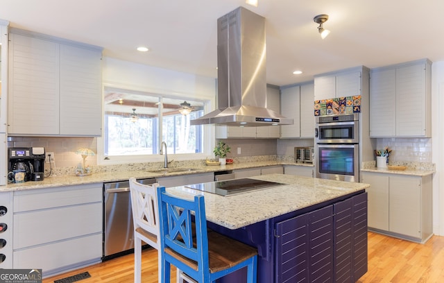 kitchen with sink, appliances with stainless steel finishes, light stone counters, island range hood, and light wood-type flooring