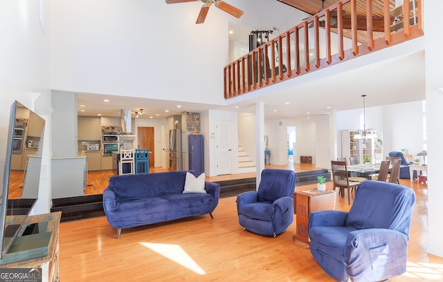 living room featuring a towering ceiling, ceiling fan with notable chandelier, and light hardwood / wood-style flooring