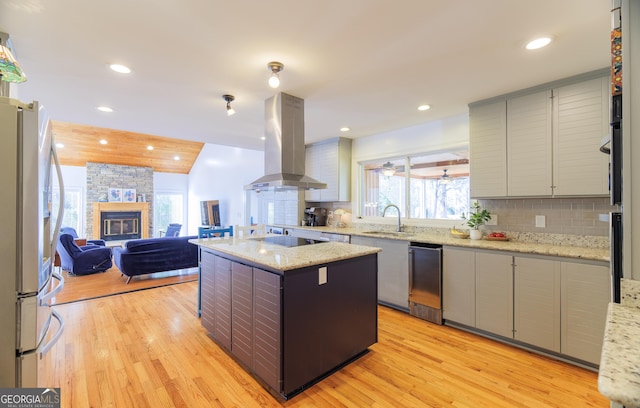 kitchen with backsplash, island exhaust hood, a center island, stainless steel fridge with ice dispenser, and light stone countertops