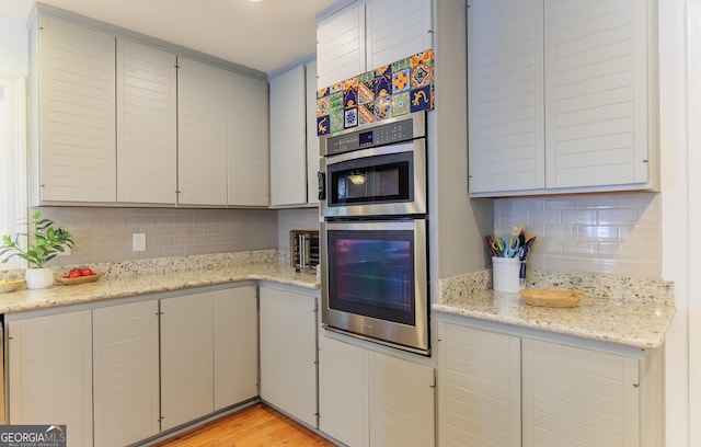 kitchen featuring tasteful backsplash, stainless steel double oven, light stone counters, and light hardwood / wood-style flooring