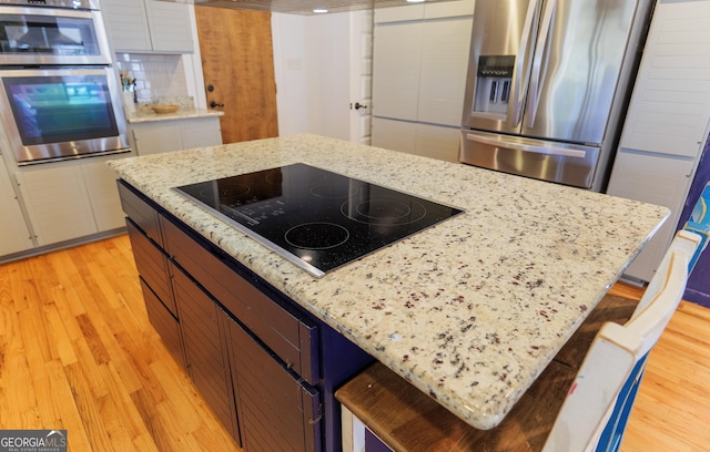 kitchen featuring stainless steel appliances, light stone countertops, a kitchen bar, and light hardwood / wood-style floors