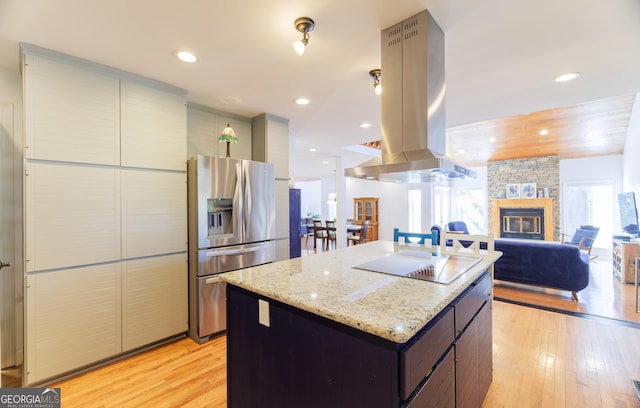 kitchen with a center island, black electric stovetop, a fireplace, island exhaust hood, and stainless steel fridge with ice dispenser