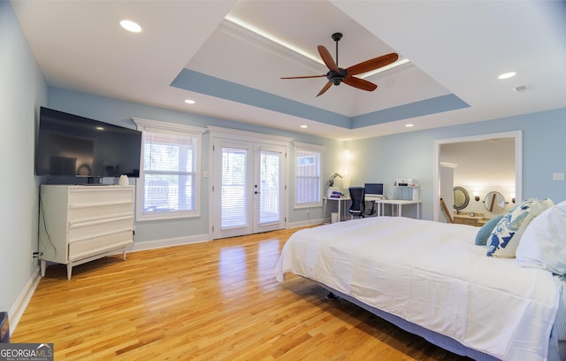 bedroom featuring french doors, light wood-type flooring, access to outside, a tray ceiling, and ceiling fan