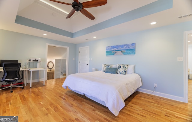 bedroom with a raised ceiling, ceiling fan, and light hardwood / wood-style floors