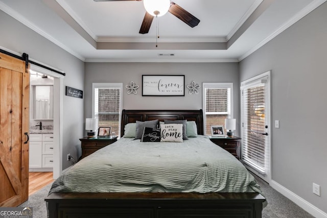 carpeted bedroom featuring a raised ceiling, ornamental molding, a barn door, and ceiling fan