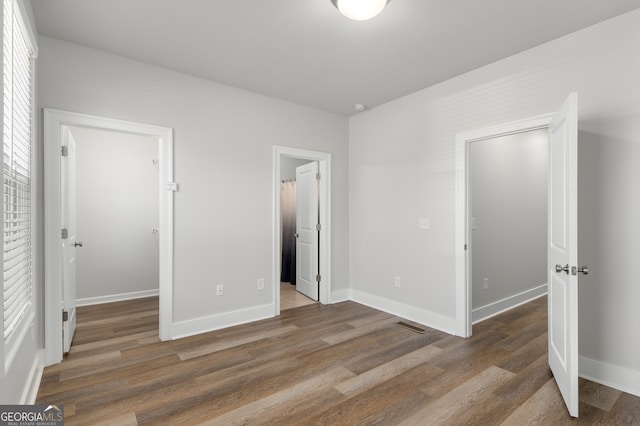 unfurnished bedroom featuring dark hardwood / wood-style flooring, ensuite bath, and a walk in closet