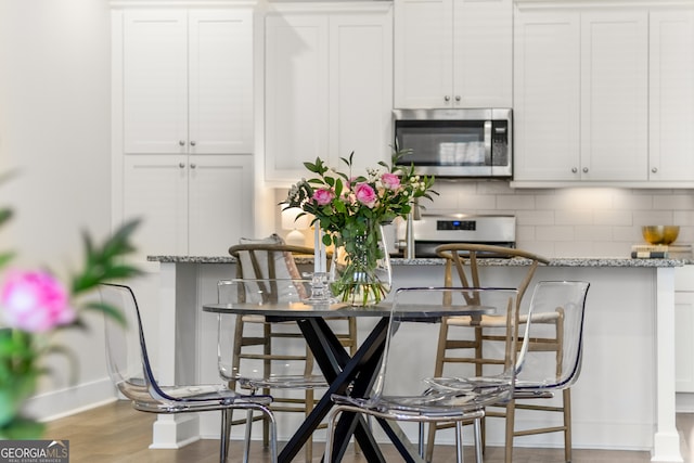 kitchen with white cabinetry, hardwood / wood-style flooring, stainless steel appliances, light stone countertops, and backsplash