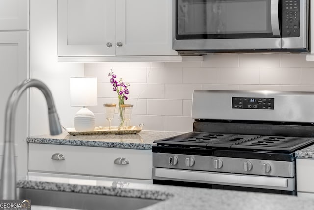 kitchen with white cabinetry, appliances with stainless steel finishes, light stone countertops, and decorative backsplash