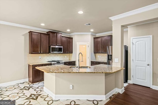 kitchen featuring sink, stainless steel appliances, light stone counters, ornamental molding, and a center island with sink