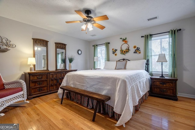 bedroom featuring ceiling fan, multiple windows, light hardwood / wood-style flooring, and a textured ceiling