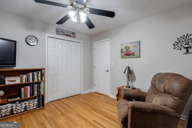 living area with ceiling fan, light hardwood / wood-style floors, and a textured ceiling