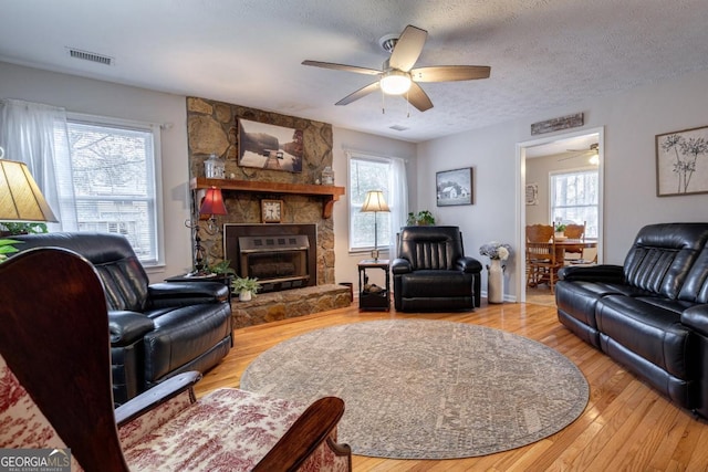 living room with ceiling fan, a fireplace, a textured ceiling, and light wood-type flooring